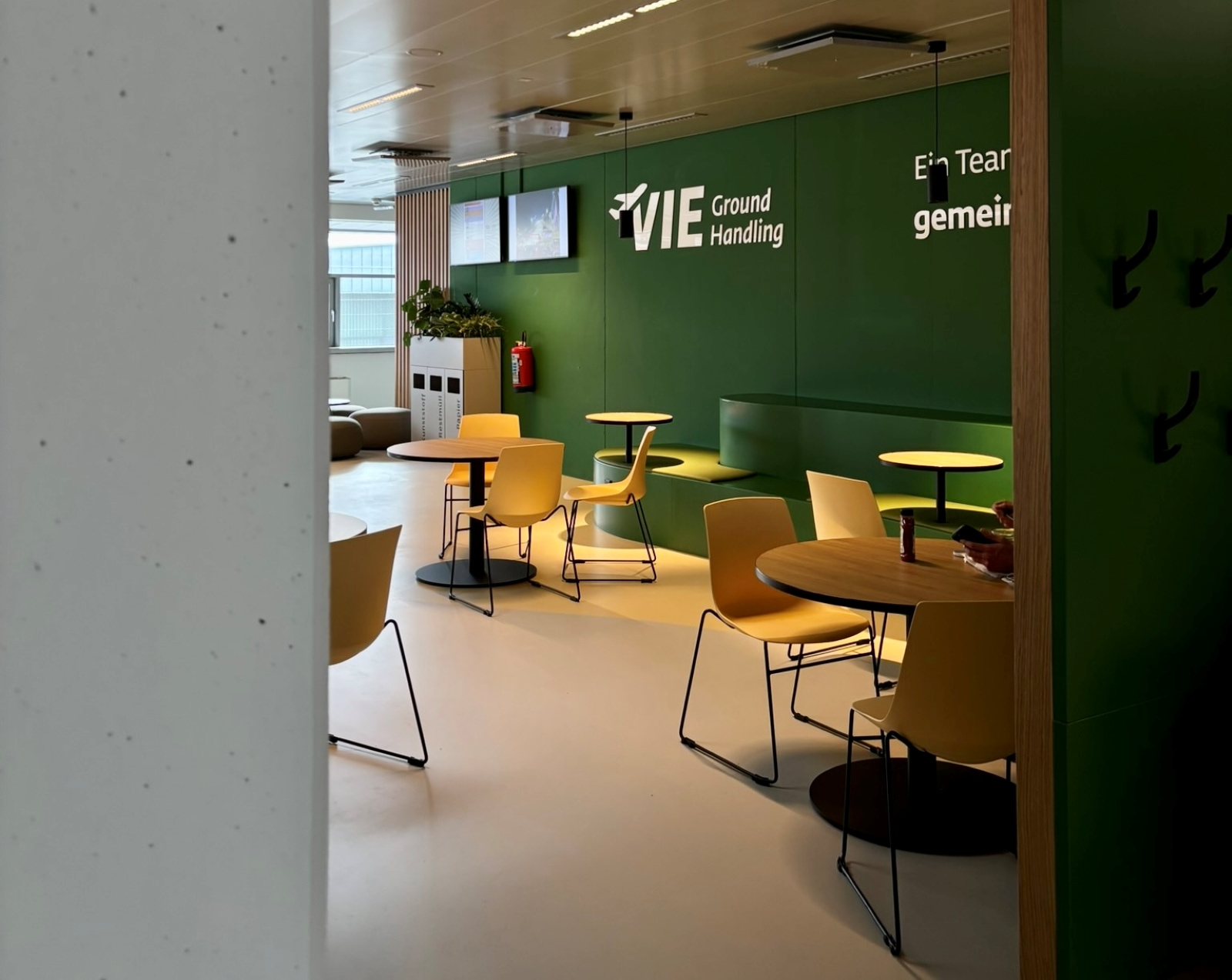 Ess- und Aufenthaltsbereich mit gelben Stühlen, grüner Wandgestaltung und VIE Ground Handling Branding.