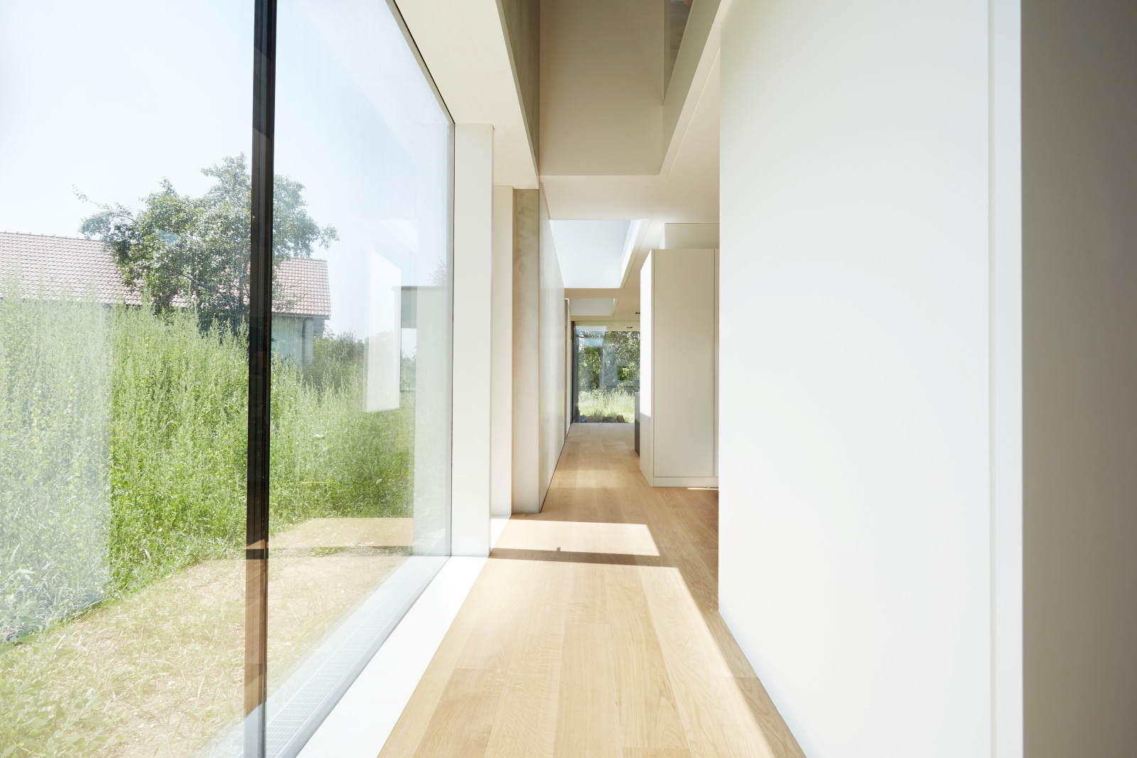 Heller Flur mit raumhohen Glasfronten und Holzfußboden – moderne Architektur verbindet Innenraum und Natur.