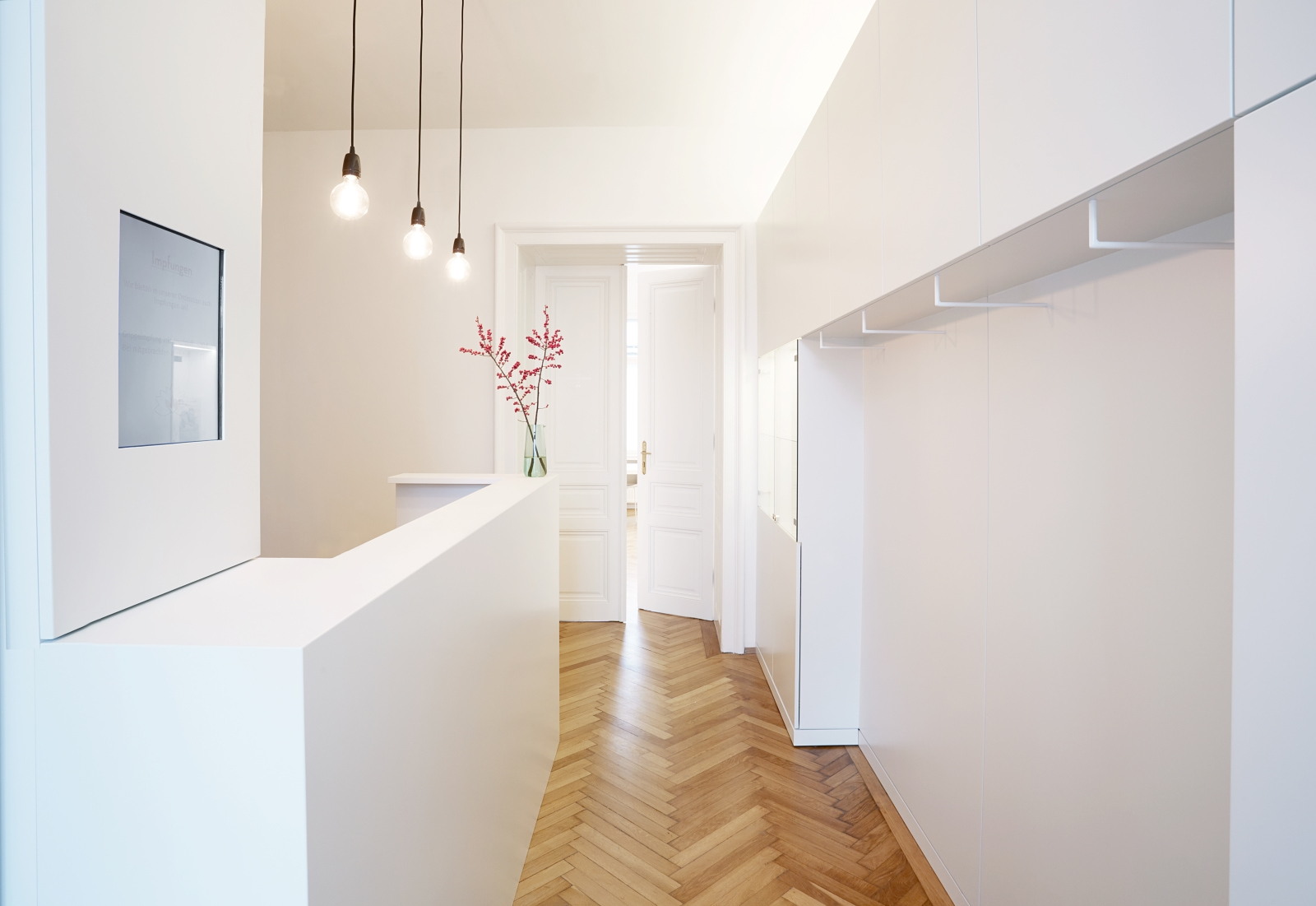 Empfangsbereich mit weißem Tresen, minimalistischen Hängependelleuchten und Parkettboden.