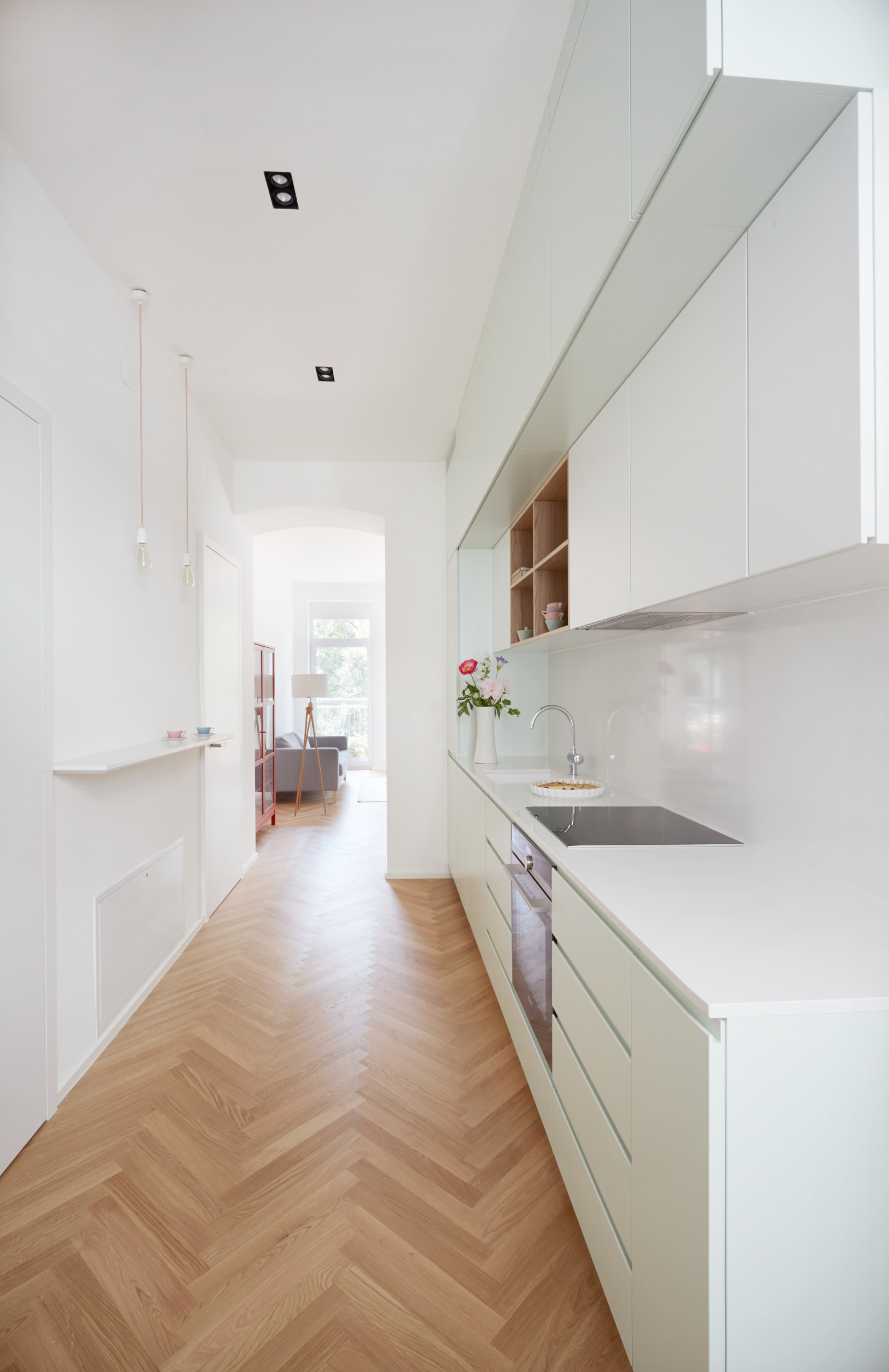 Schlanke Küchenzeile mit weißer Front und Parkettboden im Fischgrätmuster.