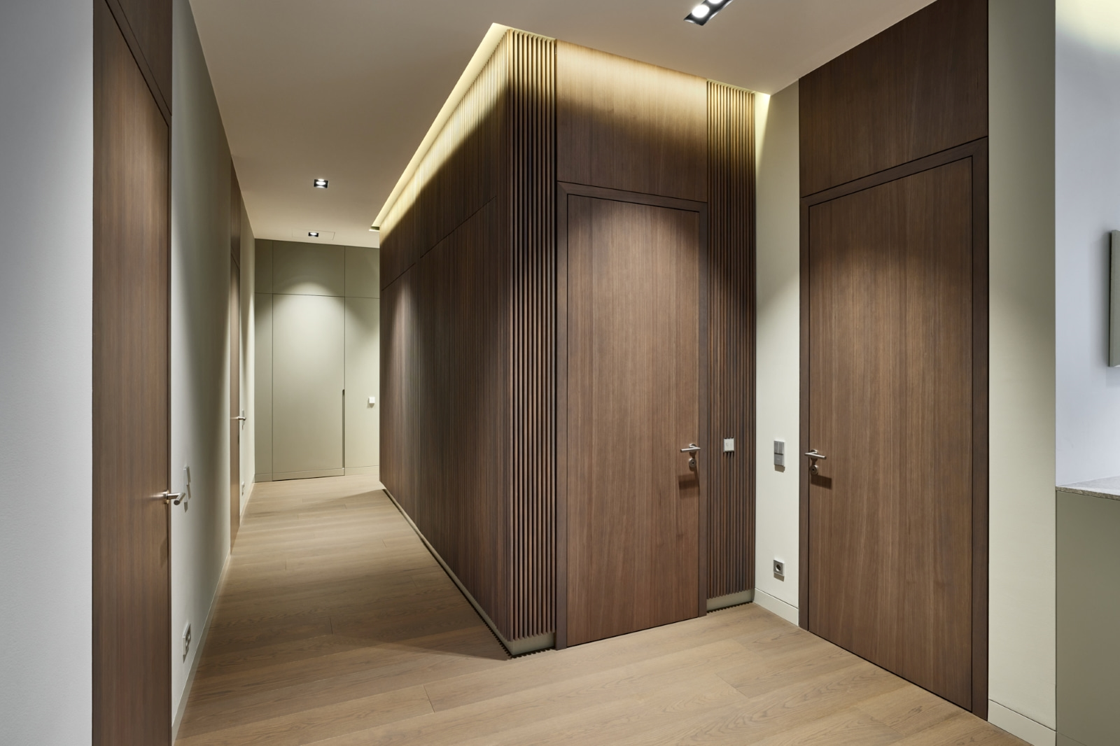Blick in den Korridor mit Holzboden, verdeckter Beleuchtung und schlichten Holzoberflächen.