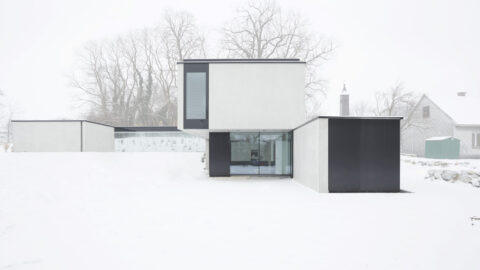 Modernes Einfamilienhaus im Winter, minimalistische Architektur mit kubischen Baukörpern in Schwarz-Weiß-Kontrast, umgeben von verschneiter Landschaft.