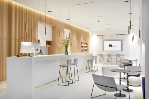 Modernes Interieur mit heller Bar und Sitzbereich, Holzlamellenwand und minimalistischer Beleuchtung, kombiniert mit eleganten Möbeln in Weiß und Grau.