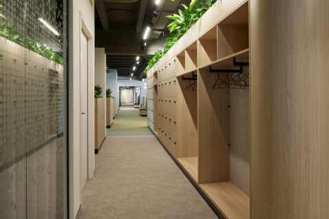Freundlicher Bürogang mit einer begrünten Locker- und Garderobenwand sowie einer Glaswand mit dezenter Folierung.