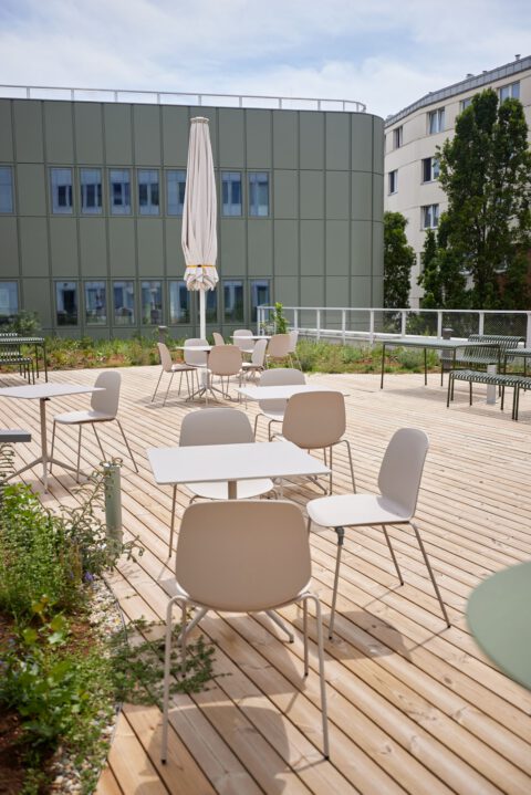 Freundliche Terrasse mit sandfarbenen und olivgrünen Möbeln, begrünten Inseln und Holzboden. Ein geschlossener Sonnenschirm ergänzt den Außenbereich.
