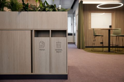 Schiebetürschrank mit integrierter Recyclingstation und Pflanzenaufsatz als multifunktionales Element im Hintergrund des Stand-up-Bereichs.