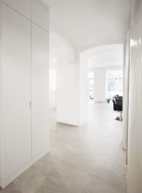 Heller Friseursalon in Wien mit minimalistischer Innenarchitektur, weißen Einbauten, offenen Rundbögen und modernem Raumkonzept von Atelier Fröhlich.