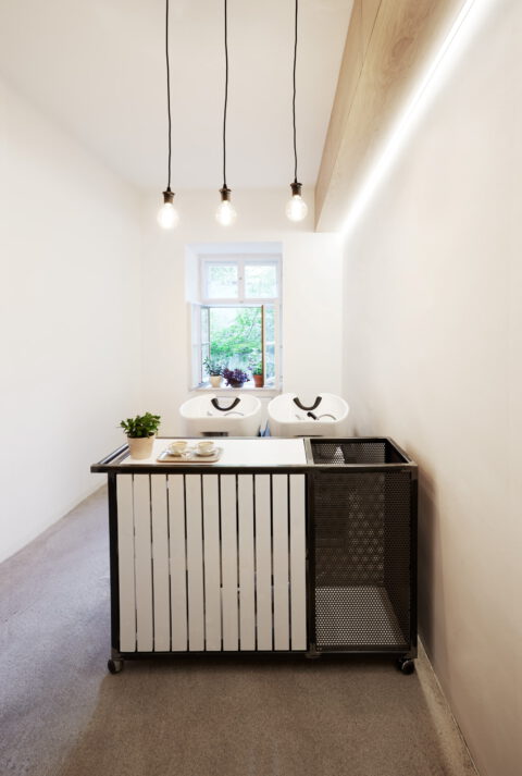 Minimalistischer Waschplatz mit industriell gestaltetem Möbel, drei Pendelleuchten und hellem Tageslicht für eine klare, moderne Atmosphäre.