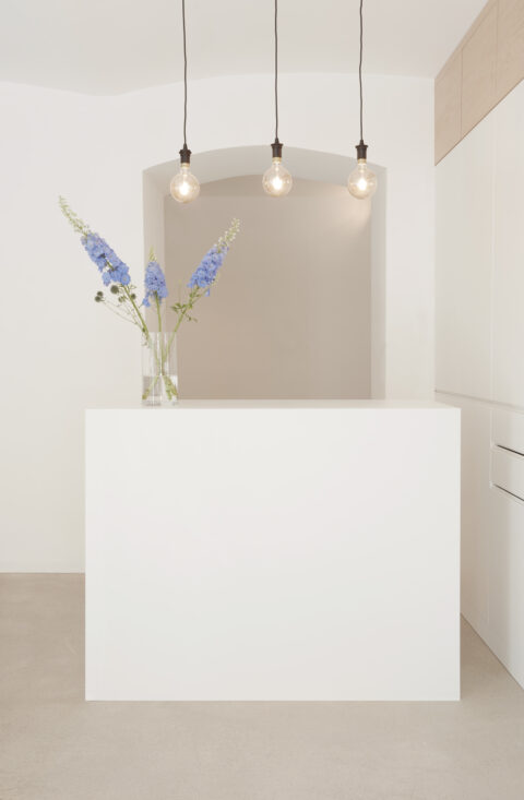 Weißer Empfangstresen mit Vase und blauen Blumen, drei Pendelleuchten und klarer, heller Raumgestaltung im Friseursalon.