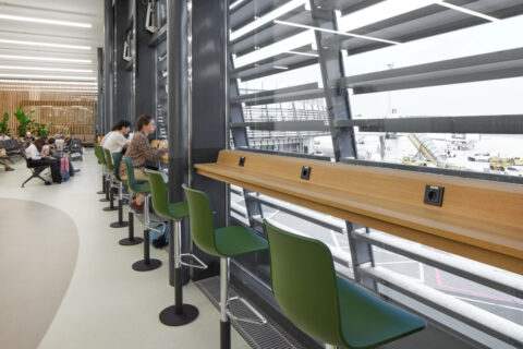 Arbeitsplätze mit Steckdosen und grünen Stühlen an der Fensterfront mit direktem Blick auf das Vorfeld.