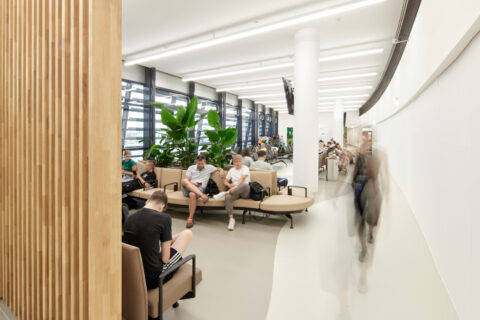 Besucherwartezone im Pier Ost mit runden Sitzgruppen, großen Pflanzeninseln und Holzlamellenwand für eine moderne, helle Atmosphäre.