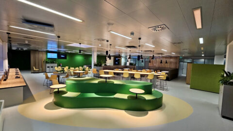 Dining area with yellow chairs, communal tables and green accents – modern architecture for break and team spaces.
