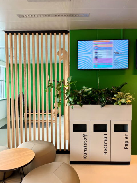 Recyclingstation mit drei Trennsystemen, Holzelementen und Begrünung als Teil des nachhaltigen Raumkonzepts.