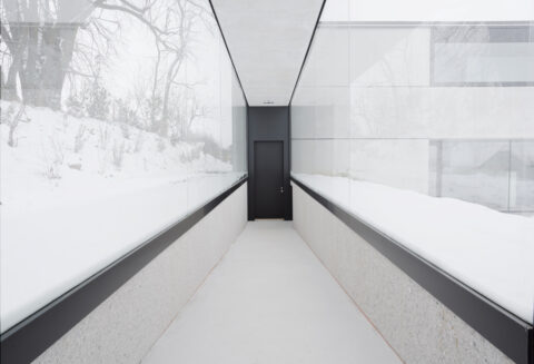 Langer Korridor mit Glaswänden, Beton und klaren Linien – minimalistisches Architekturdetail mit direktem Naturbezug.