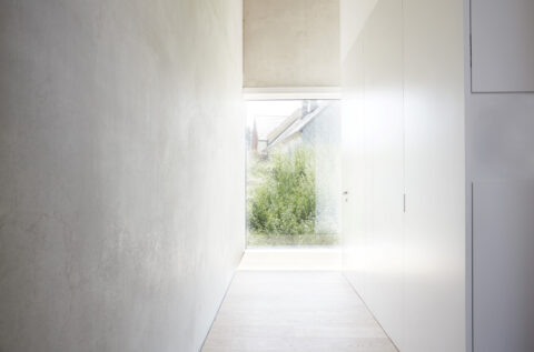 Minimalistischer Flur mit Betonwand, weißen Einbauten und großem Fenster, das natürliches Licht in den Raum lenkt.