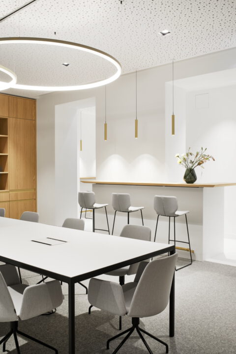 Eleganter Besprechungsraum mit kreisförmiger Lichtinstallation, minimalistischen Möbeln und heller Holzarchitektur für moderne Arbeitswelten.