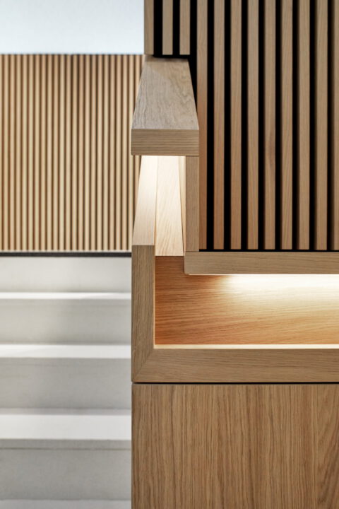 Detailaufnahme eines Holzhandlaufs mit integrierter Beleuchtung an einer modernen Treppe mit vertikaler Lamellenverkleidung.