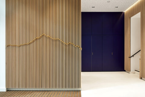 Holzlamellenwand mit goldener Kontur der Tiroler Bergkette und blauen Einbauschränken – modernes Interior Design der HYPO Tirol.