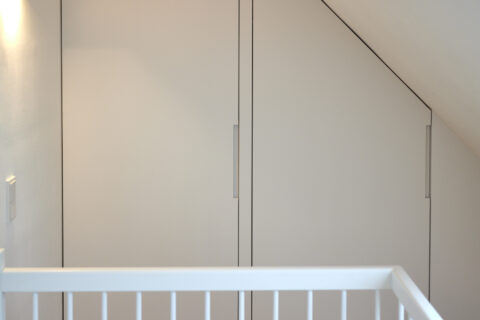 Dachgeschossausbau mit maßgefertigten weißen Schrankfronten unter der Dachschräge, minimalistische Linienführung