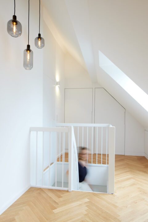 Offene Treppe mit weißem Geländer, Dachschrägenfenster und modernen Hängelampen im Dachgeschoss Wien