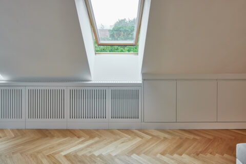 Dachgeschossausbau mit großem Dachflächenfenster, maßgefertigten Heizkörperverkleidungen und weißen Einbauten