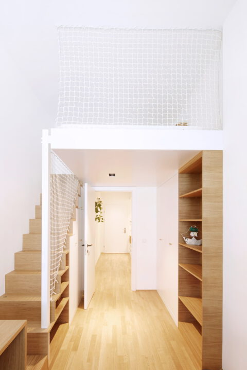 Heller Eingangsbereich mit Holztreppe, Galerie und Einbauregalen – modernes Raumkonzept mit funktionaler Architektur.