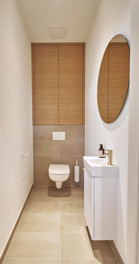 Minimalistisches WC mit Holzverkleidung und rundem Spiegel – klare architektonische Gestaltung.