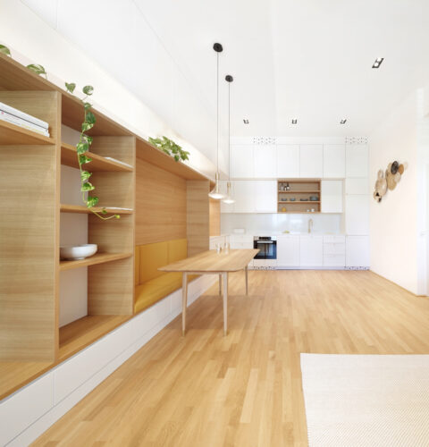 Offener Wohnraum mit Küche, Holzeinbauten und Sitzbank – funktionales Design mit klarer architektonischer Struktur.