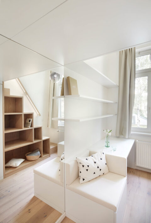 Kompakte Wohnlösung mit Sitzbank, Regalen und Spiegelwand unterhalb eines Hochbetts im Apartment.