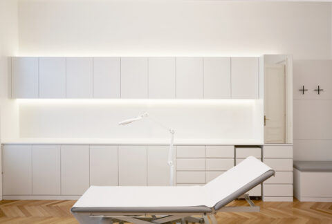 Behandlungszimmer mit weißem Behandlungstisch, raumhohen Schränken und indirekter Beleuchtung.