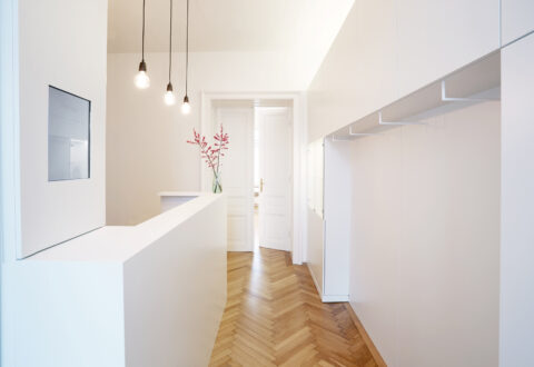 Empfangsbereich mit weißem Tresen, minimalistischen Hängependelleuchten und Parkettboden.