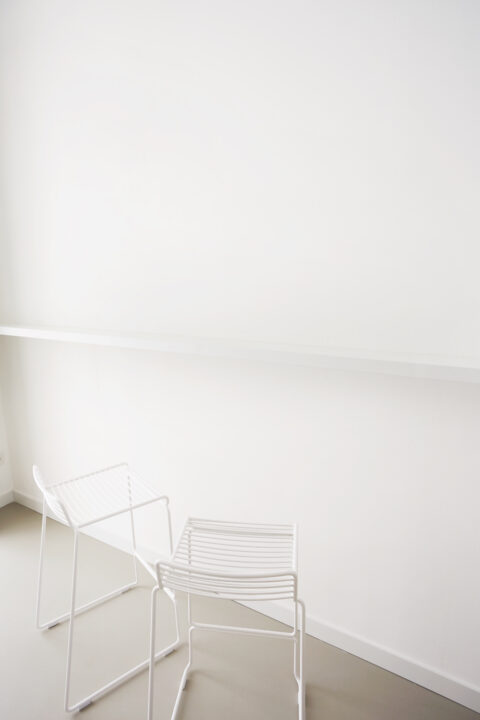 Zwei weiße Barhocker vor einer minimalistischen weißen Wand im Wohnbereich.