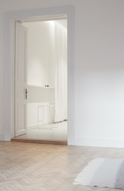 Blick vom Wohnzimmer durch die offene Tür zur weißen Küche im Trennmöbel.