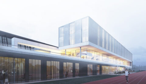 Modernes Sportzentrum mit großen Glasfassaden, hell beleuchteten Innenräumen und einer Laufbahn im Vordergrund, auf der Personen trainieren.