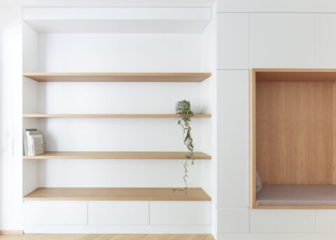 Weißes Wandregal mit Holzböden und integrierter Sitznische.