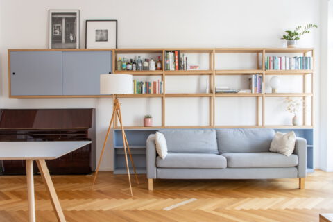 Innenansicht eines Wohnzimmers mit maßgefertigtem Regalsystem, blau-grauen Elementen und Sofa.