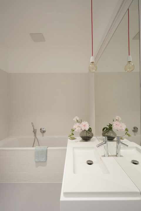 Nahaufnahme des Badezimmers mit Badewanne, Spiegelwand und modernen Leuchten.