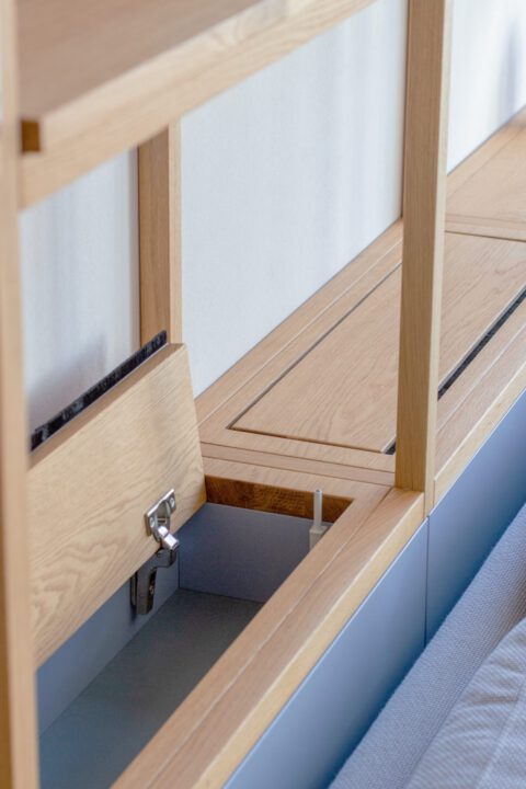 Detailansicht des Regals mit verstecktem Stauraum und Klappe – clevere Aufbewahrungslösung aus hochwertigem Holz.
