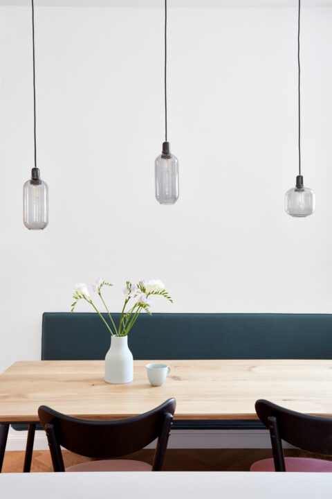 Essbereich mit Holztisch, schwarzem Stühlen, Vase mit Blumen und drei Pendelleuchten