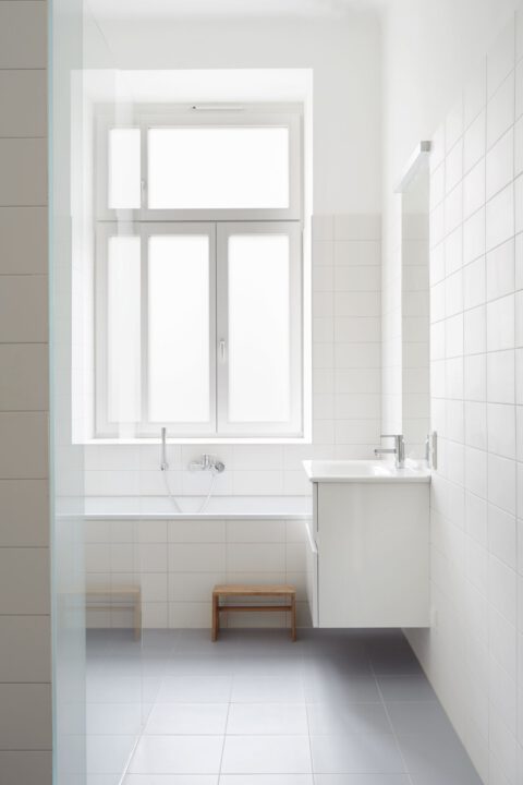 Helles Badezimmer mit Badewanne unter einem großen Milchglasfenster, weißen Fliesenwänden und einem modernen Waschbecken.