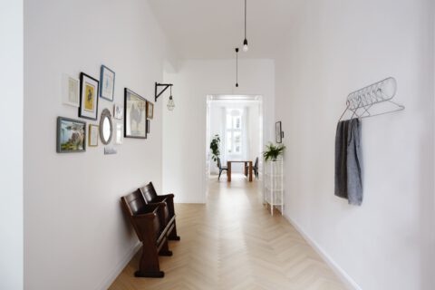 Heller Vorraum mit Fischgrätparkett, dekorierter Bilderwand, zwei alten Holzsitzen und Ausblick in einen lichtdurchfluteten Essbereich.