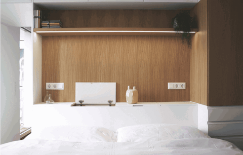 Innenansicht des Bettes mit weißer Bettwäsche und hölzerner Rückwand mit Regal.