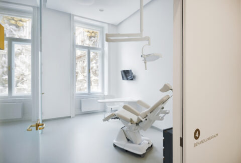 Behandlungszimmer mit Zahnarztstuhl, großem Fenster und modernem Interieur.