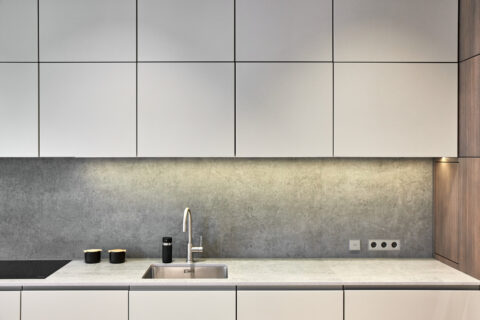 Küchenzeile mit grauen Fronten, Kunststeinrückwand und integrierter Beleuchtung.