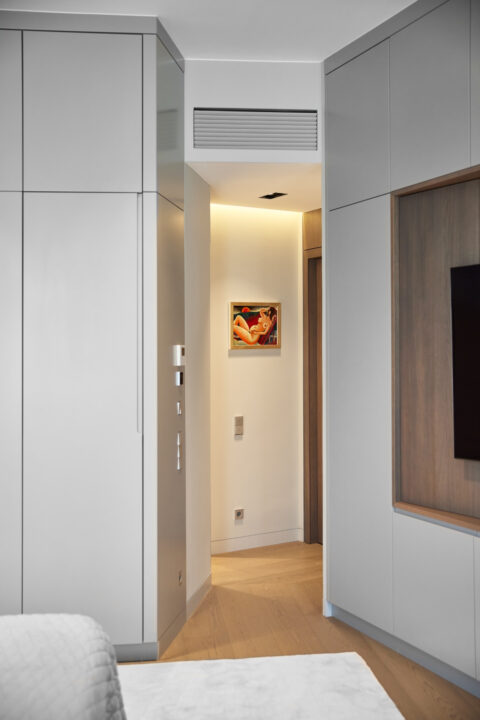 Blick in ein Schlafzimmer mit maßgefertigten Einbauten in Grau und Holz, integrierter TV-Nische und Blick in den Flur.