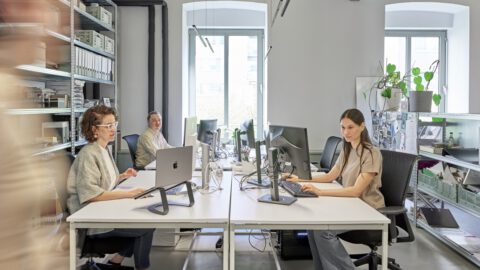 Team at Atelier Froehlich in the office, three people are sitting at their workstations, one person is walking past.