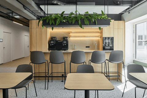 Freundliche Cafeteria als sozialer Mittelpunkt mit begrünter Hängeleuchte, langer Theke, Barstühlen und Essbereichen.